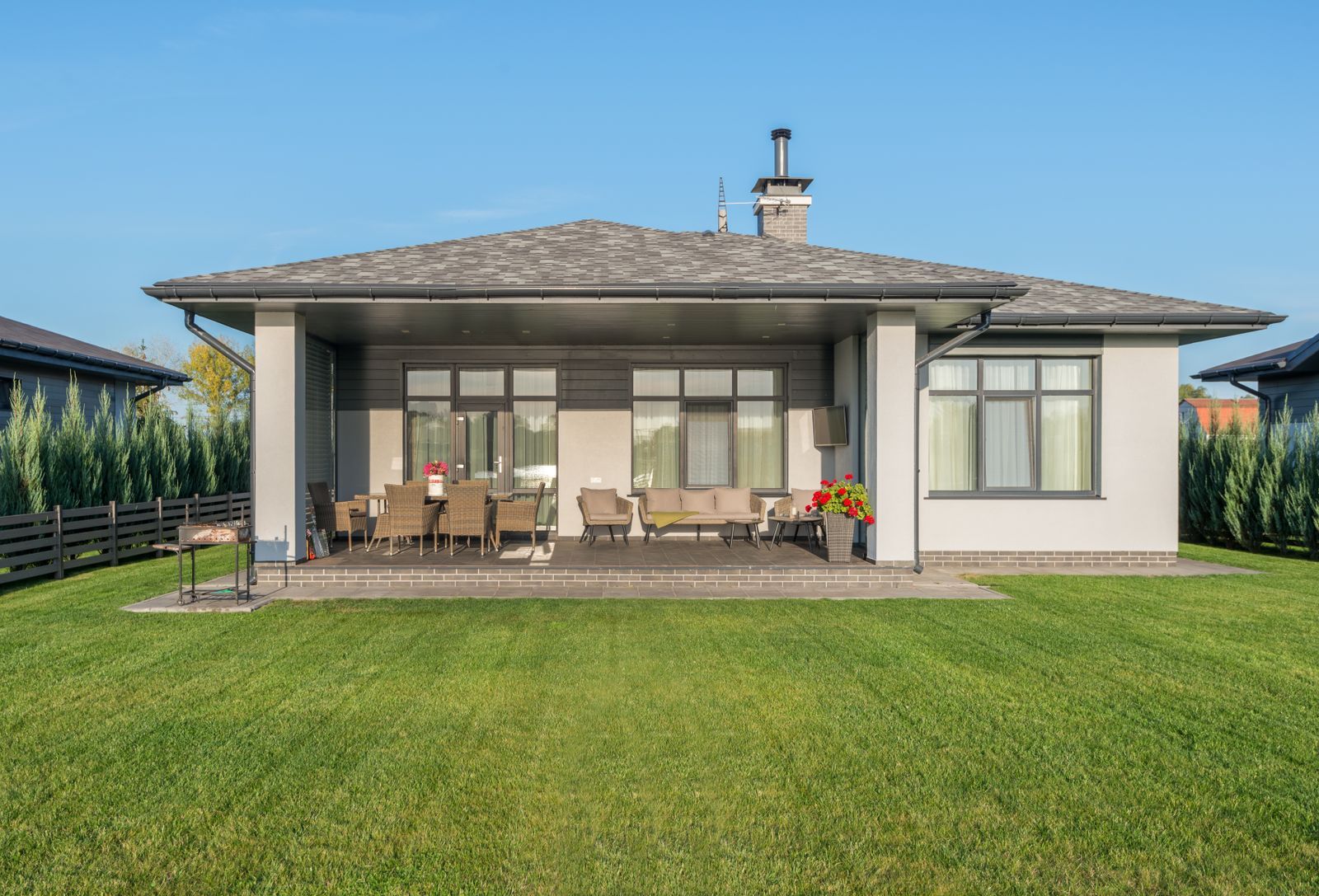A wide green lawn in front of a house with a covered patio and outdoor furniture