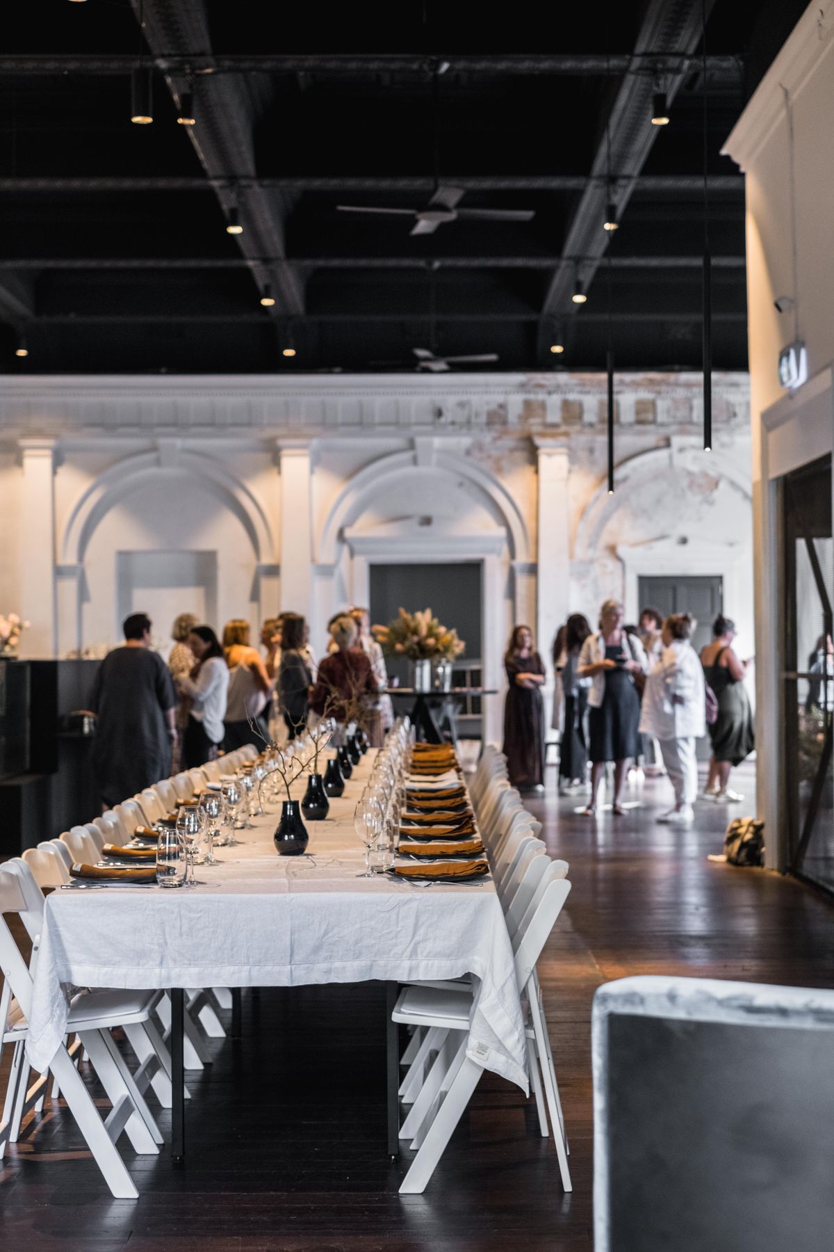 Guests mingling at a function in a large white room with long tables