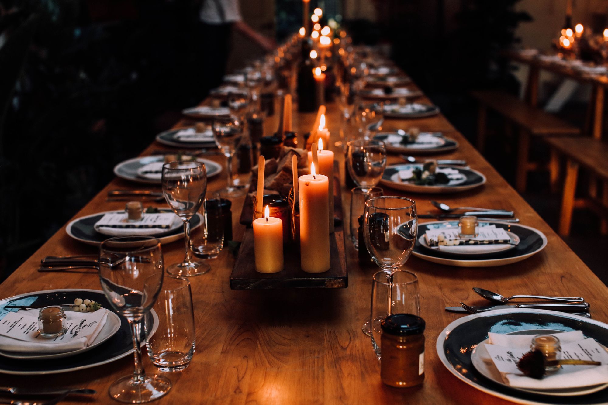 A candlelit table set for dinner with dark plates and glasses