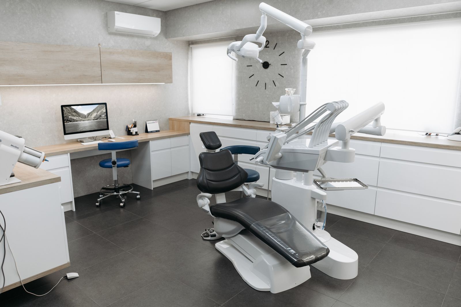 A bright treatment room with a grey dental chair and white cabinetry