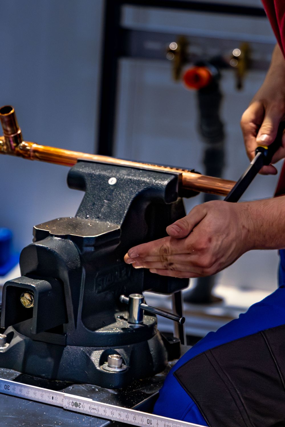 A plumber bending copper pipe in a bench vice