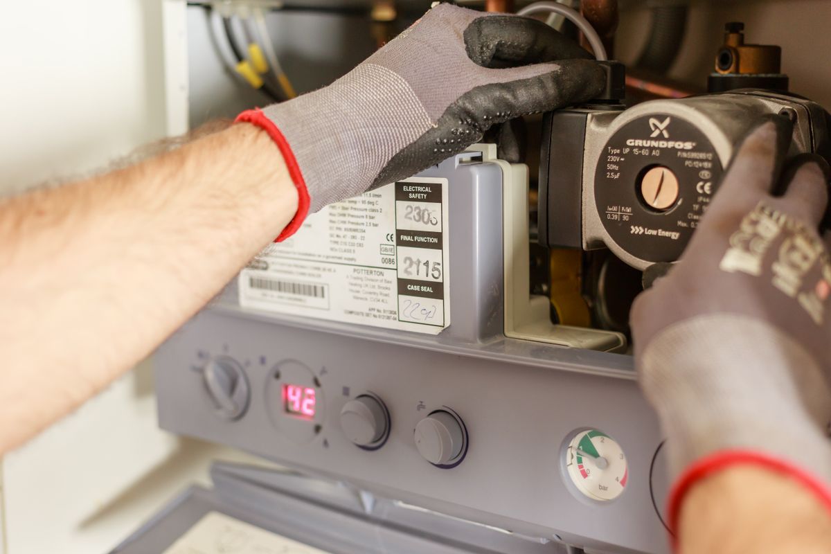 Hands in work gloves servicing a hot water unit