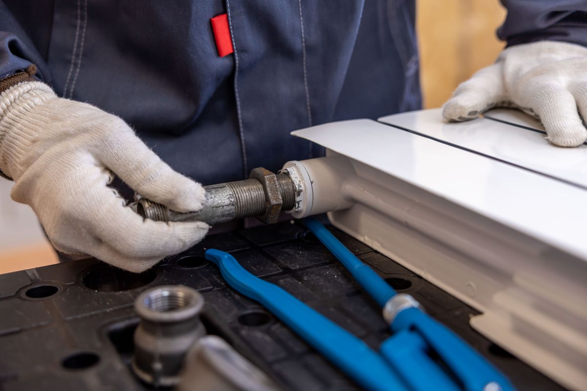 Gloved hands fitting a valve to a radiator pipe