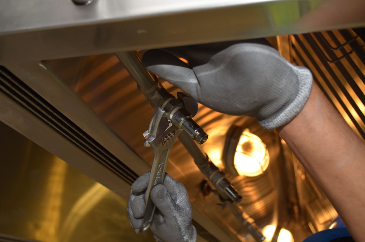A plumber's gloved hands using a spanner on pipework under warm light