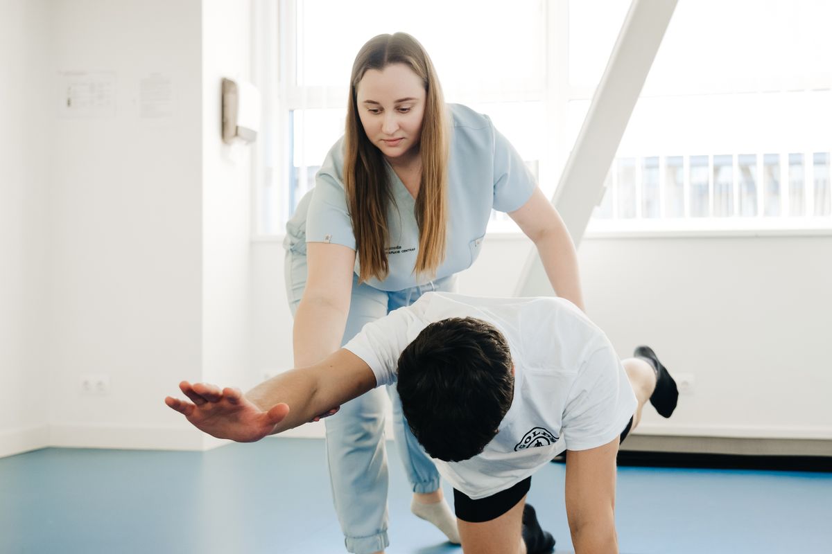 A physio guiding a patient through a balance exercise on the clinic floor