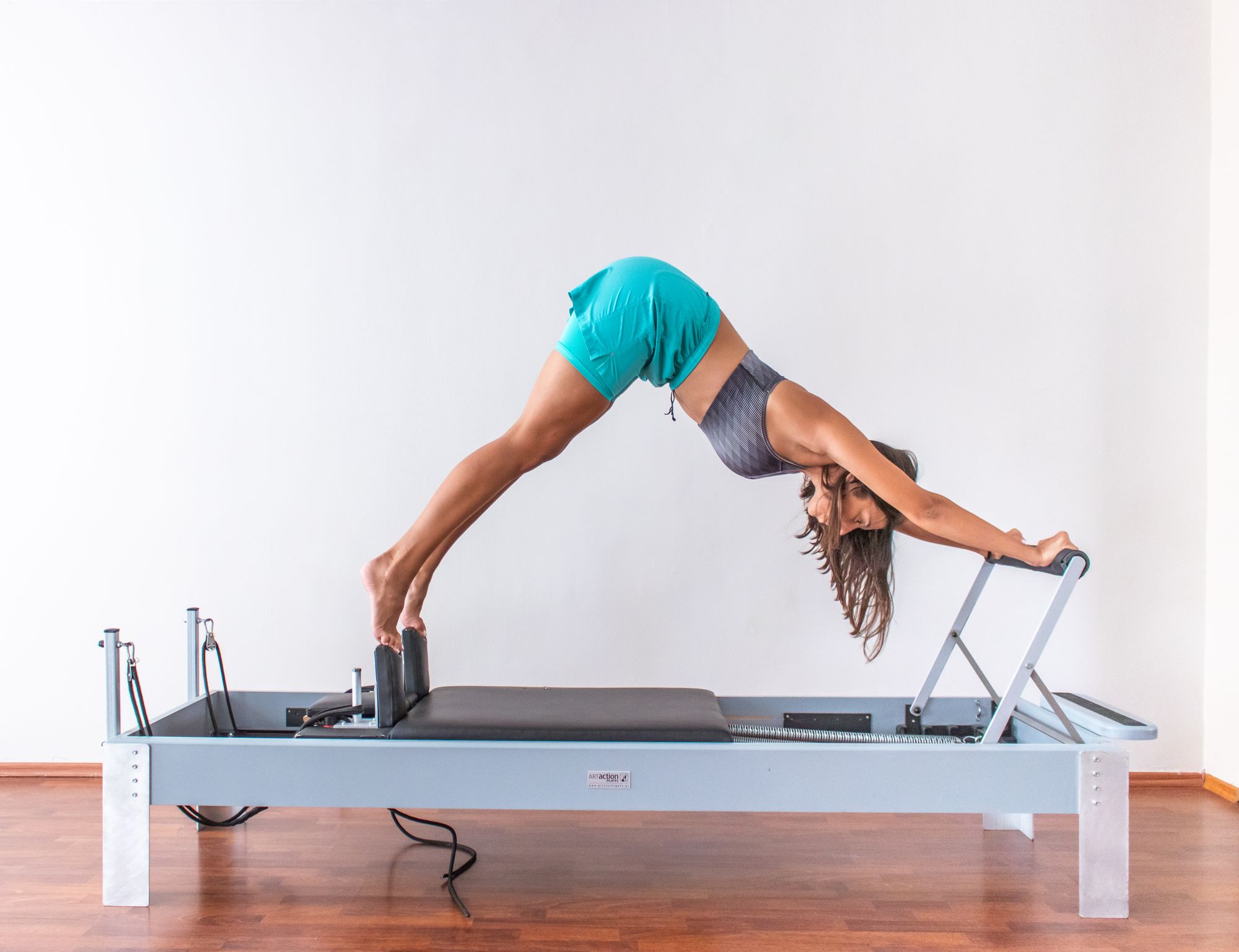 A woman holding a pike position on a reformer in a white studio