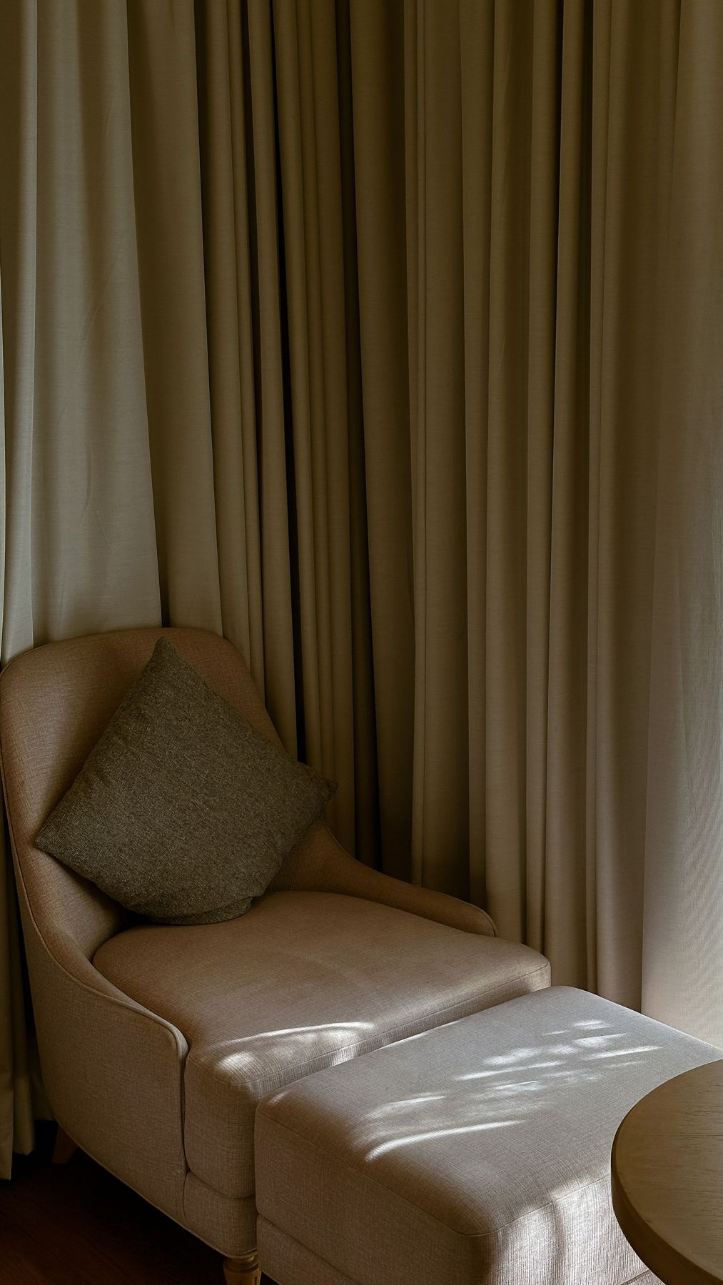 A soft armchair beside long curtains in a quiet room
